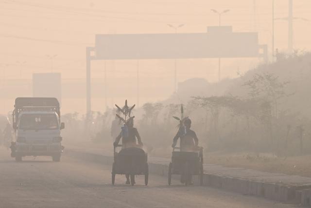 Vendors (R) push their carts as they sell corn along a street engulfed in smog in Lahore on October 25, 2025. (Photo by Arif ALI / AFP)