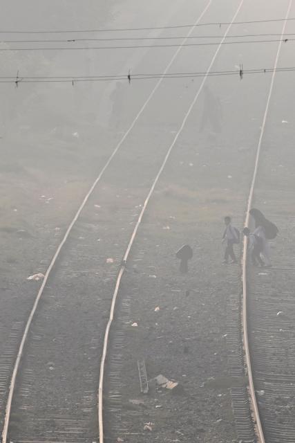 People walk across a railway track amid smoggy conditions in Lahore on October 25, 2025. (Photo by Arif ALI / AFP)