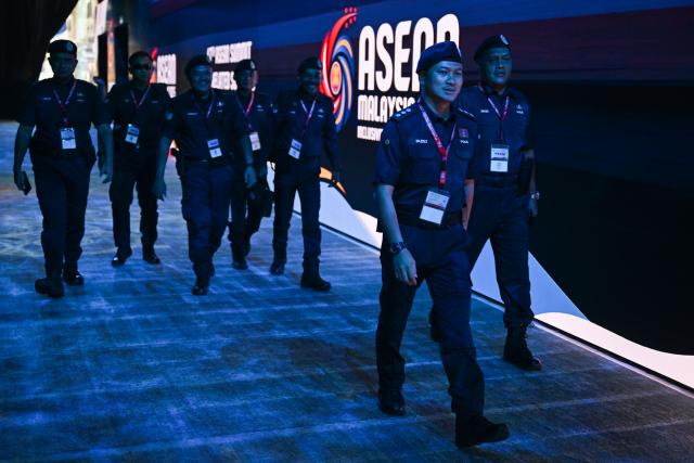 Members of the Royal Malaysia Police walk next to the Association of Southeast Asian Nations (ASEAN) logo ahead of the 47th ASEAN Summit in Kuala Lumpur on October 25, 2025. US President Donald Trump arrives in Malaysia on October 26 for the Association of Southeast Asian Nations (ASEAN) summit -- a meeting he skipped several times in his first term. (Photo by Mohd RASFAN / AFP)
