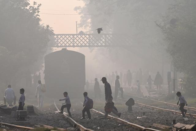 People walk across a railway track amid smoggy conditions in Lahore on October 25, 2025. (Photo by Arif ALI / AFP)