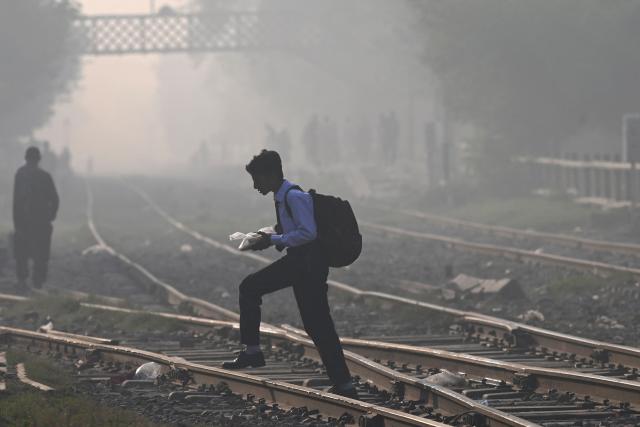 A school boy walks across a railway track amid smoggy conditions in Lahore on October 25, 2025. (Photo by Arif ALI / AFP)
