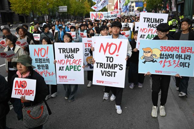 Protesters carry placards as they march during a rally, condemning US President Donald Trump's pressure for increased South Korean investment in the US, in Seoul on October 25, 2025. Trump headed for Asia on October 25 and high-stakes trade talks with Chinese counterpart Xi Jinping, saying that he would also like to meet North Korean leader Kim Jong Un on his trip. (Photo by Jung Yeon-je / AFP)
