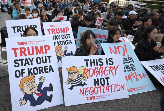 Protesters hold placards during a rally, condemning US President Donald Trump's pressure for increased South Korean investment in the US, in Seoul on October 25, 2025. Trump headed for Asia on October 25 and high-stakes trade talks with Chinese counterpart Xi Jinping, saying that he would also like to meet North Korean leader Kim Jong Un on his trip. (Photo by Jung Yeon-je / AFP)