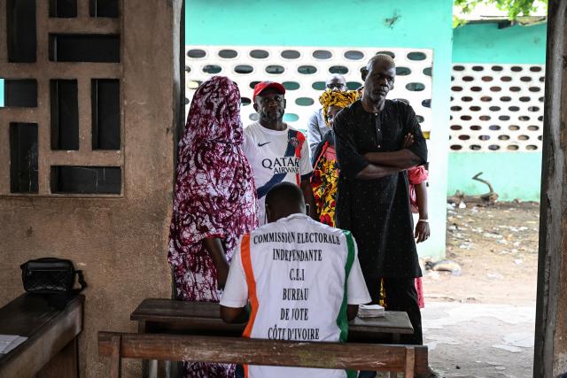 An Independent Electoral Commission of Ivory Coast (CEI) official assists voters at the Kenedy school group polling station in Cocody, Abidjan, on October 25, 2025 during Ivory Coast's presidential elections. (Photo by SIA KAMBOU / AFP)
