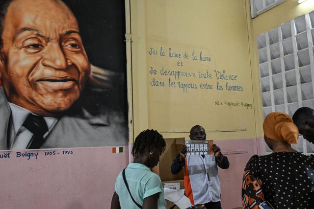 Independent Electoral Commission of Ivory Coast (CEI) officials count votes at the Notre-Dame College, where a painting of Ivory Coast's first President Felix Houphouet-Boigny is seen on a wall, in Plateau, the business district of Abidjan, on October 25, 2025 after polls closed during Ivory Coast's presidential elections. (Photo by Sia KAMBOU / AFP)