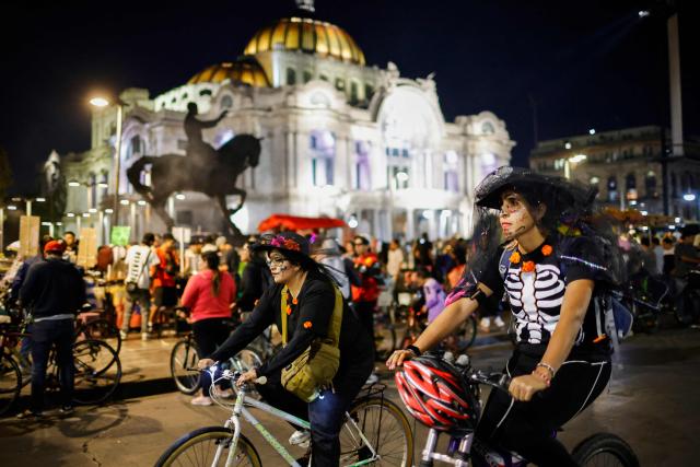 Cyclists in costumes ride past the Palacio de Bellas Artes during a nighttime ride ahead of the Day of the Dead ("Dia de los Muertos") celebrations in Mexico City on October 25, 2025. (Photo by Rodrigo Oropeza / AFP)