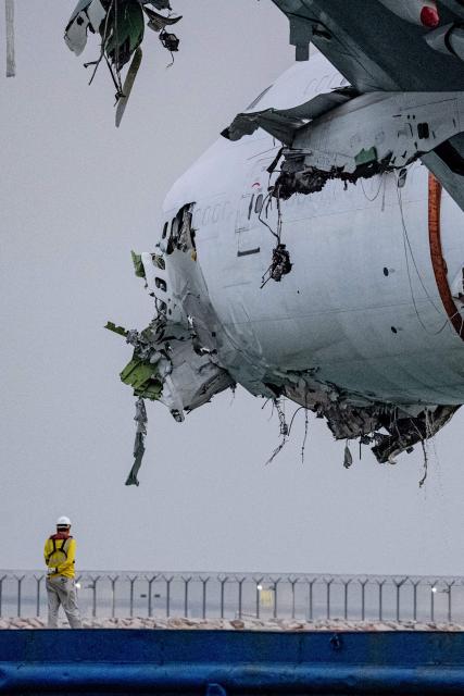 A salvage worker looks on as the main fuselage section of an ACT Airlines Boeing 747-400 cargo aircraft, wet leased by Emirates SkyCargo, is hoisted out of the water in Hong Kong on October 26, 2025, after it veered off an airport runway on October 20 during landing, hitting a security patrol car and then skidding into the sea, leaving two men in the vehicle dead. (Photo by Leung Man Hei / AFP)