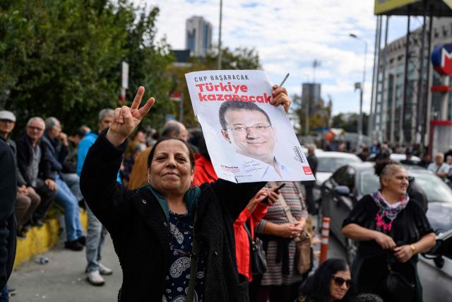 A protester flashes the peace symbol and holds a poster with the picture of jailed Istanbul Mayor Ekrem Imamoglu during a rally organized by the country's main opposition party, the Republican People's Party (CHP), to protest the suspension and imprisonment of Istanbul Mayor, in Istanbul on October 26, 2025. Istanbul's opposition mayor was detained on March 19, 2025 and jailed several days later as part of a corruption investigation, a move that sparked Turkey's worst street protests in over a decade. (Photo by Yasin AKGUL / AFP)