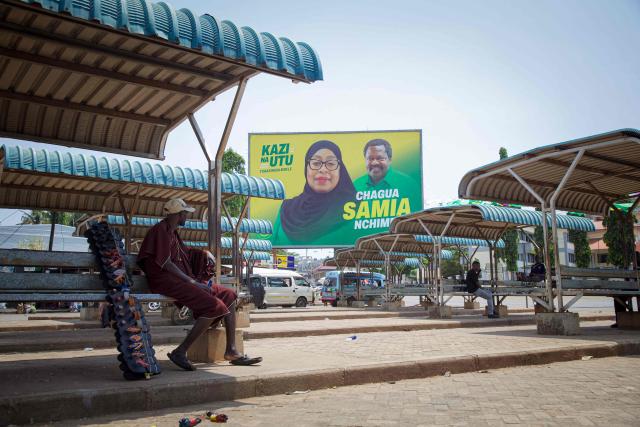A Masai man sits next to a billboard of ruling Tanzanian Chama Cha Mapinduzi (CCM - Revolutionary Party) of the incumbent President Samia Suluhu Hassan in Kigoma town on October 26, 2025. (Photo by AFP)