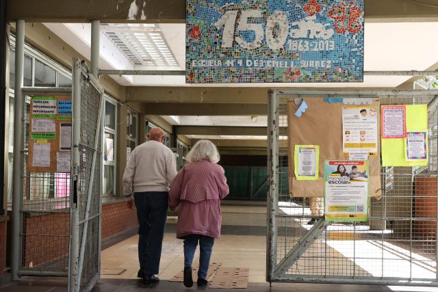 A couple enters a polling station to vote during the national midterm legislative election in Buenos Aires on October 26, 2025. Argentines head to the polls for a midterm election that will determine whether President Javier Milei enters the second half of his term bolstered or diminished as economic troubles abound despite unprecedented US aid. (Photo by Alejandro PAGNI / AFP)