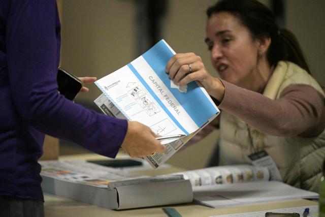 A woman receives a paper ballot from a polling station official during the national midterm legislative election in Buenos Aires on October 26, 2025. Argentines head to the polls for a midterm election that will determine whether President Javier Milei enters the second half of his term bolstered or diminished as economic troubles abound despite unprecedented US aid. (Photo by JUAN MABROMATA / AFP)