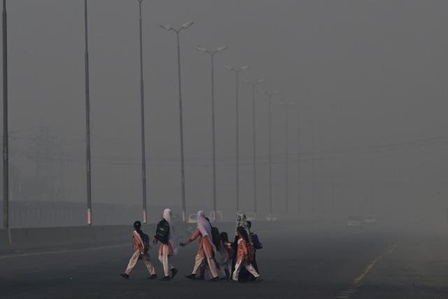 School children cross a road amid dense smog in Lahore on October 27, 2025. (Photo by Arif ALI / AFP)