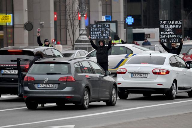 Activists hold placards as they demonstrate among stopped cars at Independence Square in Kyiv on October 27, 2025, during a "National Minute of Silence for Those Who Died" as a result of Russia's armed aggression against Ukraine. (Photo by Sergei SUPINSKY / AFP)