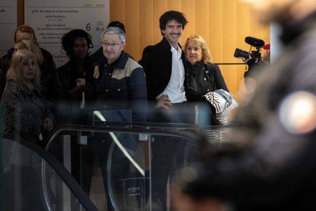 French lawyer Juan Branco (C) looks on at the Paris courthouse on the sidelines of the trial opening of ten people accused of sexist cyber-harassment of Brigitte Macron, in Paris, on October 27, 2025. Ten people go on trial in Paris on October 27, 2025 for sexist cyber-harassment of Brigitte Macron, in the latest case sparked by unsubstantiated gender claims thrown at the wife of the French President for years by some in France and beyond. (Photo by Guillaume BAPTISTE / AFP)