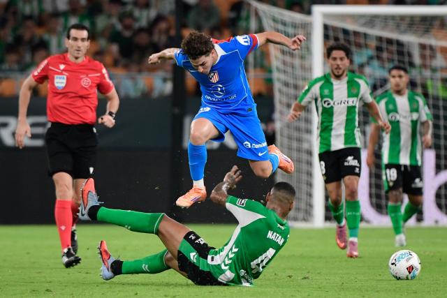 Atletico Madrid's Argentine forward #19 Julian Alvarez (top) leaps over Real Betis' Brazilian defender #04 Natan Bernardo de Souza during the Spanish league football match between Real Betis and Club Atletico de Madrid at the Cartuja Stadium in Seville on October 27, 2025. (Photo by CRISTINA QUICLER / AFP)