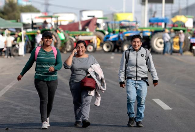 People walk in front of tractors from Jalisco farmers blocking the highway to Nogales to protest the price of corn and against the federal government in Zapopan, Jalisco state, Mexico on October 27, 2025. (Photo by ULISES RUIZ / AFP)