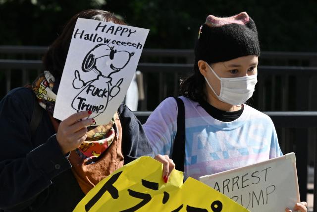 Two anti-Trump protesters hold signs near the Akasaka Palace, where US President Donald Trump was meeting Japanese Prime Minister Sanae Takaichi, in Tokyo on October 28, 2025. (Photo by GREG BAKER / AFP)