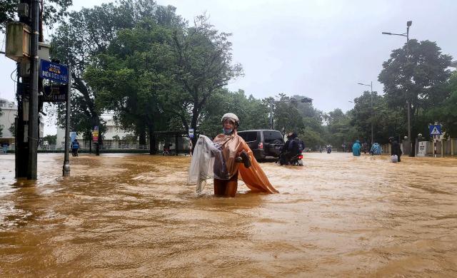 TOPSHOT - A woman wearing a raincoat wades through a flooded street in Hue on October 28, 2025. The central Vietnamese city of Hue recorded more than a metre of rainfall in a 24-hour period, smashing a national record set over two decades ago, the environment ministry said. (Photo by AFP)