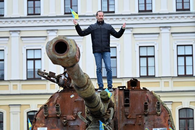 A man holding a Ukraine's national flag poses for photos on a Russian self-propelled gun at the open air exhibition of destroyed Russian equipment in Kyiv on October 28, 2025, amid the Russian invasion of Ukraine. (Photo by Sergei SUPINSKY / AFP)