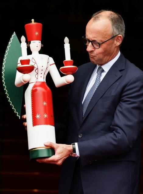 German Chancellor Friedrich Merz holds a traditional wodden candleholder offered to him by the Miners' Music Corps (Bergmannsmusikkorps) as he arrives at Saxony's State Chancellery in Dresden, eastern Germany, on October 28, 2025, during Merz' official first visit as a Chancellor to the eastern federal state of Saxony.  (Photo by JENS SCHLUETER / AFP)