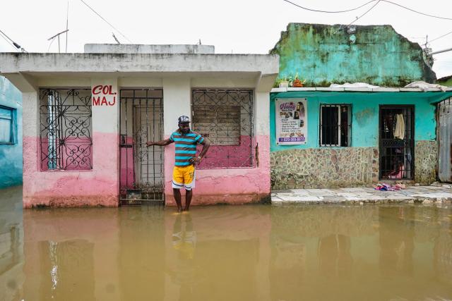 A man stands next to a house on a flooded street ahead of the arrival of Hurricane Melissa at Las Cucarachas neighborhood in Santo Domingo, Dominican Republic on October 28, 2025. (Photo by Danny Polanco / AFP)