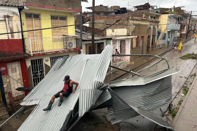 A resident slides over part of the roof of his house, damaged by Hurricane Melissa, in Santiago de Cuba on October 29, 2025. A powerful Hurricane Melissa made landfall in eastern Cuba on Wednesday, causing damage and flooding to homes and streets in Santiago de Cuba province, an AFP team on the ground reported. (Photo by YAMIL LAGE / AFP)