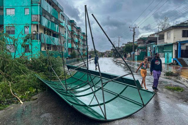 Residents walk past debris and fallen trees after Hurricane Melissa struck Santiago de Cuba on October 29, 2025. A powerful Hurricane Melissa made landfall in eastern Cuba on Wednesday, causing damage and flooding to homes and streets in Santiago de Cuba province, an AFP team on the ground reported. (Photo by YAMIL LAGE / AFP)