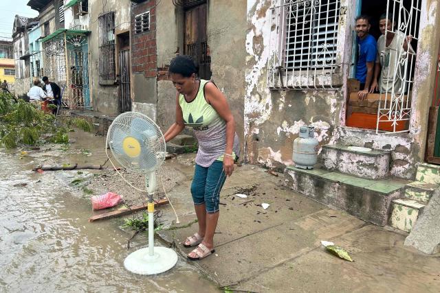 A woman uses water from a flooded street to clean her fan after Hurricane Melissa struck in Santiago de Cuba on October 29, 2025. A powerful Hurricane Melissa made landfall in eastern Cuba on Wednesday, causing damage and flooding to homes and streets in Santiago de Cuba province, an AFP team on the ground reported. (Photo by YAMIL LAGE / AFP)