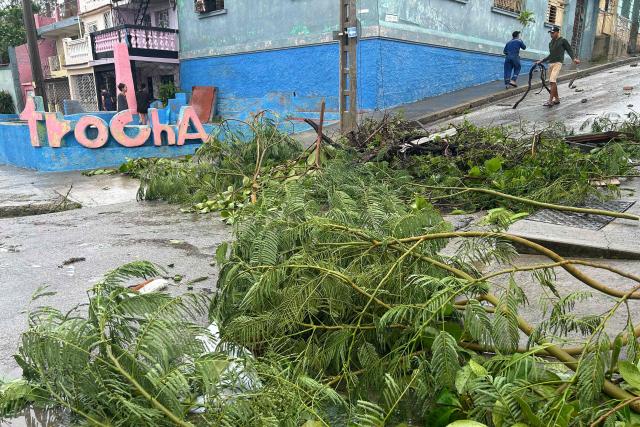 People walk down a street covered with fallen tree branches after Hurricane Melissa struck in Santiago de Cuba on October 29, 2025. A powerful Hurricane Melissa made landfall in eastern Cuba on Wednesday, causing damage and flooding to homes and streets in Santiago de Cuba province, an AFP team on the ground reported. (Photo by YAMIL LAGE / AFP)