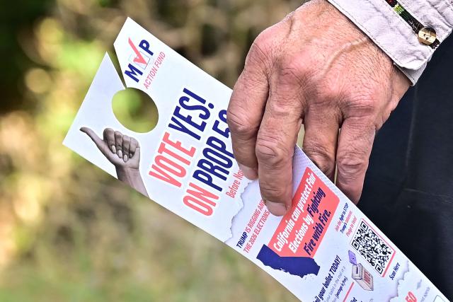 Veteran canvasser Fernando Flores holds door hangers promoting Vote Yes on Prop 50 while canvassing a neighborhood  of Los Angeles on October 22, 2025 ahead of the November 4 election. In the heart of Los Angeles, a team of canvassers is tirelessly knocking on doors, asking voters to let California redraw its electoral map to favor Democrats and resist Donald Trump. (Photo by Frederic J. BROWN / AFP)