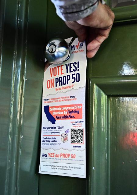 Veteran canvasser Fernando Flores hangs a door hanger at a home where no one answered promoting Vote Yes on Prop 50 while canvassing a neighborhood in Los Angeles on October 22, 2025 ahead of the November 4 election. In the heart of Los Angeles, a team of canvassers is tirelessly knocking on doors, asking voters to let California redraw its electoral map to favor Democrats and resist Donald Trump. (Photo by Frederic J. BROWN / AFP)