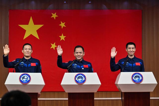 Astronauts for China's Shenzhou-21 space mission Zhang Hongzhang (L), Commander Zhang Lu (C) and Wu Fei (R) wave during a press conference a day before the launch of the mission at the Jiuquan Satellite Launch Centre in the Gobi desert, in northwest China on October 30, 2025. (Photo by Hector RETAMAL / AFP)