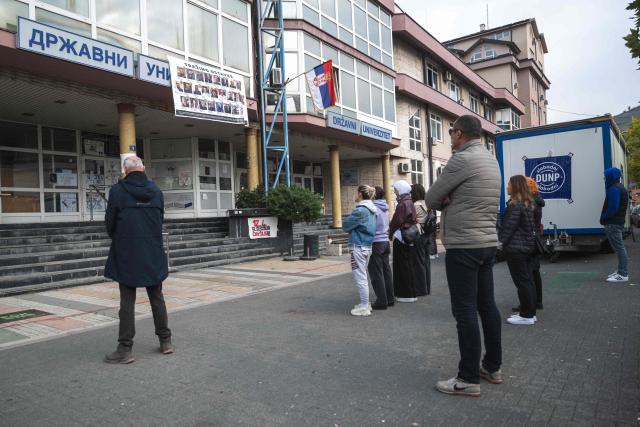 People stand still silently for 16 minutes before the blocked university, paying tribute to the 16 victims in the city of Novi Pazar, South-western Serbia, on October 22, 2025. Serbia is preparing to mark the first anniversary of the Novi Sad tragedy, which sparked some of the biggest protests in its history — a year that left the country deeply changed and polarised.
The train-station collapse in the country’s second-largest city, which killed 16 people just months after renovation, became a symbol of entrenched corruption — bringing hundreds of thousands to the streets under the "bloody hand" stencil that became its emblem. (Photo by Andrej ISAKOVIC / AFP)