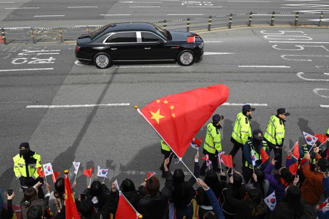 A motorcade of China's President Xi Jinping drives past Chinese people gathered to welcome him outside an air base at Gimhae International Airport in Busan on October 30, 2025, as he arrives to attend the Asia-Pacific Economic Cooperation (APEC) Summit. (Photo by Jung Yeon-je / AFP)