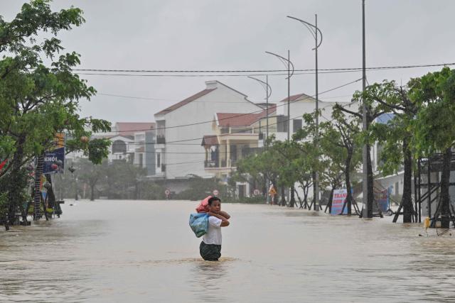 A man carries belongings as he wades through a flooded street during heavy rains in Hoi An on October 30, 2025. Vietnam's coastal provinces have been lashed by heavy rains since October 26, with a record of up to 1.7 metres (five feet seven inches) falling over 24 hours. (Photo by NHAC NGUYEN / AFP)