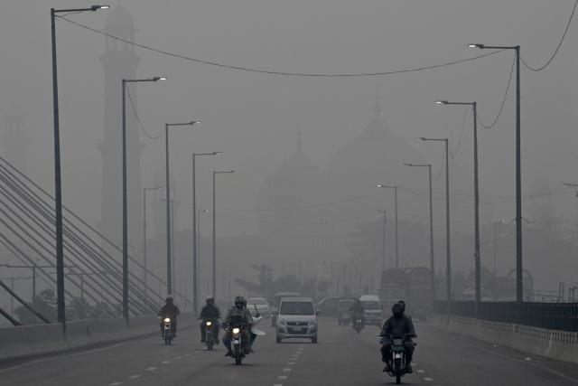 Commuters ride along a road amid dense smog in Lahore on October 30, 2025. (Photo by Arif ALI / AFP)