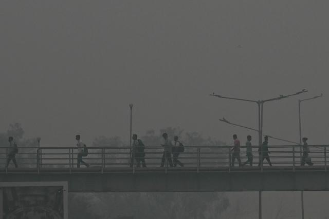 Commuters walk across a footbridge amid smoggy conditions in New Delhi on October 30, 2025. (Photo by Arun SANKAR / AFP)