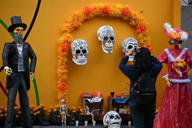 Visitors take pictures in front of an altar with skulls, skeletons, and Catrinas dedicated to the Day of the Dead in Mexico City on October 30, 2025. (Photo by Yuri CORTEZ / AFP)