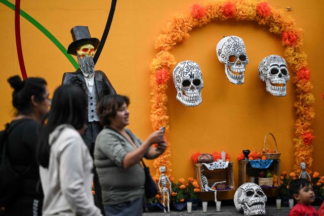 Visitors take pictures in front of an altar with skulls, skeletons, and Catrinas dedicated to the Day of the Dead in Mexico City on October 30, 2025. (Photo by Yuri CORTEZ / AFP)