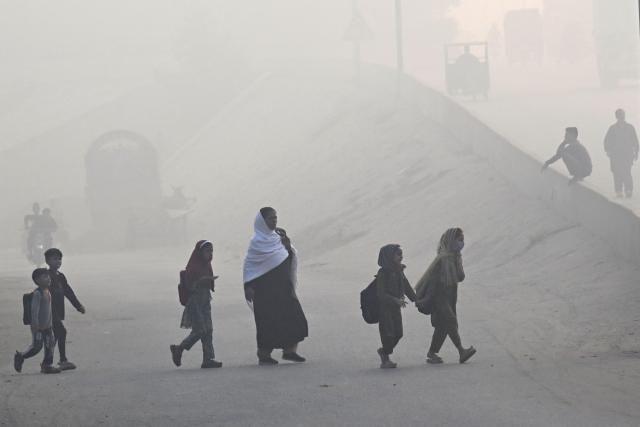 TOPSHOT - School children walk across a road amid dense smog in Lahore on October 31, 2025. (Photo by Arif ALI / AFP)