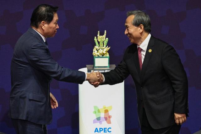 Chairman of the China Council for the Promotion of International Trade Ren Hongbin (R) shakes hands with SK Group Chairman Chey Tae-won during the Asia-Pacific Economic Cooperation (APEC) CEO Summit at the Gyeongju Arts Center in Gyeongju on October 31, 2025. (Photo by ANTHONY WALLACE / AFP)