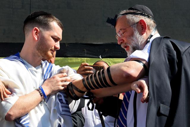 Bar Kupershtein (L), one of the former Israeli hostages held in the Gaza Strip since the October 7, 2023 attack by the Palestinian militant group Hamas, takes part in the Jewish Tefillin ceremony giving thanks for his safe return and to pray for the returns of the bodies of the remaining hostages still thought to be under the rubble of Gaza, in Hostages Square, in Tel Aviv on October 31, 2025. Under the truce deal, Israel is to return the remains of 15 Palestinians for every deceased Israeli hostage returned by Hamas. The militant group insists it is committed to the ceasefire plan but is struggling to find the 10 remaining dead because two years of Israeli bombardments have erased Gazan landmarks. (Photo by Jack GUEZ / AFP)