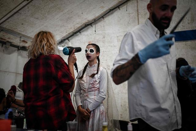 A woman dries the makeup of a performer dressed in a Halloween costume at the volunteer-run haunted house attraction featuring horror-themed decorations for Halloween in Ambes, on the outskirts of Bordeaux, south-western France, on October 31, 2025. The seasonal horror attraction, which opens exclusively on Halloween, marks its 10th anniversary this year with an expanded venue after creator Antoine Vignaud took a year off to prepare this special edition. (Photo by Philippe LOPEZ / AFP)