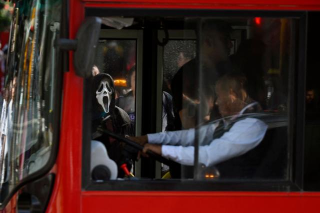 A man wearing a mask of the film character Ghostface waits for the public transport ahead of the Day of the Dead celebration on Reforma Avenue in Mexico City on October 31, 2025. (Photo by Alfredo ESTRELLA / AFP)
