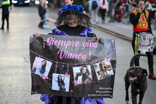 A woman with her face painted as "Catrina" holds a banner with a victim during a protest march to demand the clarification of femicides ahead of the Day of the Dead celebrations in Mexico City on October 31, 2025. (Photo by Yuri CORTEZ / AFP)