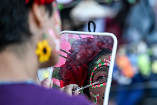 A woman makes up her face as she prepares to participate in a protest march to demand the clarification of femicides ahead of the Day of the Dead celebrations in Mexico City on October 31, 2025. (Photo by Yuri CORTEZ / AFP)