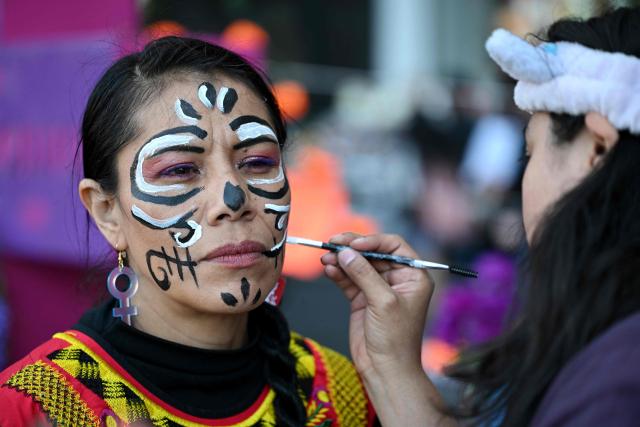 A woman makes up her face as she prepares to participate in a protest march to demand the clarification of femicides ahead of the Day of the Dead celebrations in Mexico City on October 31, 2025. (Photo by Yuri CORTEZ / AFP)