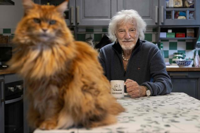 (FILES) French singer, songwriter, and composer Hugues Aufray enjoys a coffee in the kitchen of his house with his cat Lily, in Marly-le-Roi near Paris, on October 14, 2025. "Santiano", "Céline", "Stewball"...: crowned with timeless successes, including adaptations of his friend Bob Dylan's songs, Hugues Aufray, a guiding figure in Francophone music, continues his journey with undiminished energy and embarks on a new tour at the age of 96. (Photo by JOEL SAGET / AFP)