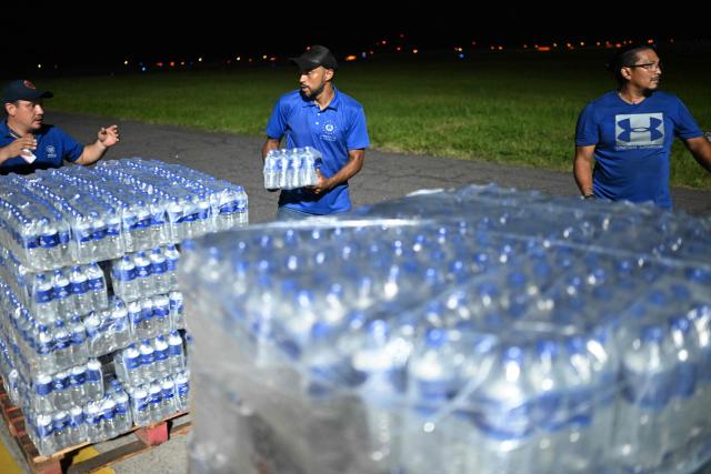 Salvadorean government workers prepare pallets with bottled water to load in a plane with humanitarian aid bound for Jamaica, ordered by El Salvador's President Nayib Bukele, after the passage of Hurricane Melissa, at the tarmac of San Oscar Romero International Airport in San Luis Talpa, El Salvador on October 31, 2025. Melissa, the worst Atlantic hurricane in nearly a century, left at least 30 dead in Haiti and 19 in Jamaica, as well as parts of Cuba in ruins, as it moved through the Caribbean toward Bermuda on Thursday. (Photo by Marvin RECINOS / AFP)
