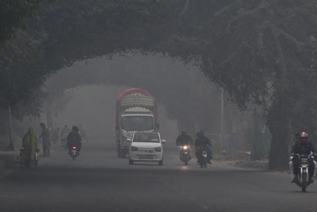 Commuters ride along a street amid dense smog in Lahore on November 1, 2025. (Photo by Arif ALI / AFP)